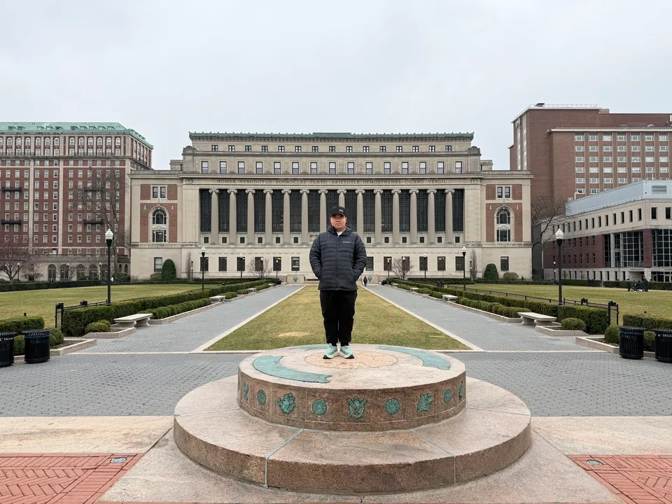 Jinhao standing on a round stone plinth on a campus lawn, a columned library behind