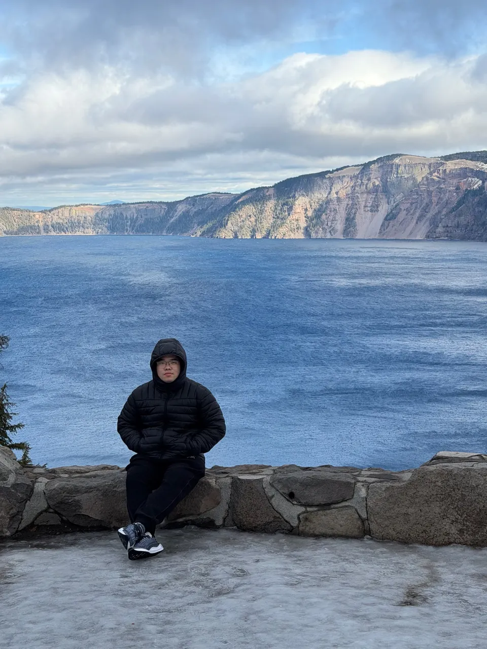 Jinhao sitting on a stone wall above the deep blue Crater Lake