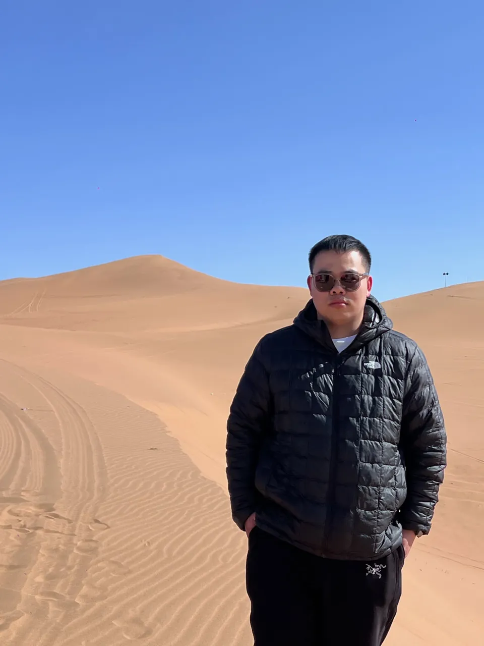 Jinhao in a black jacket on a sand dune under a clear sky