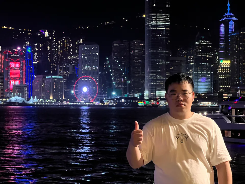 Jinhao with a thumbs up in front of the lit Hong Kong skyline at night