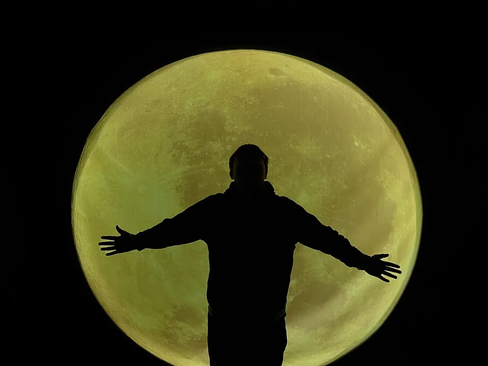 Silhouette with arms open in front of a huge full moon