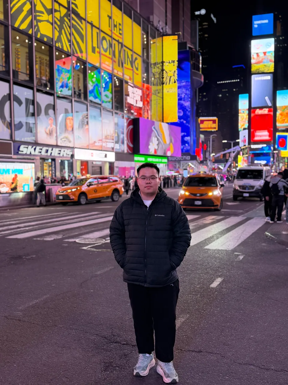 Jinhao on a crosswalk in Times Square at night under bright billboards