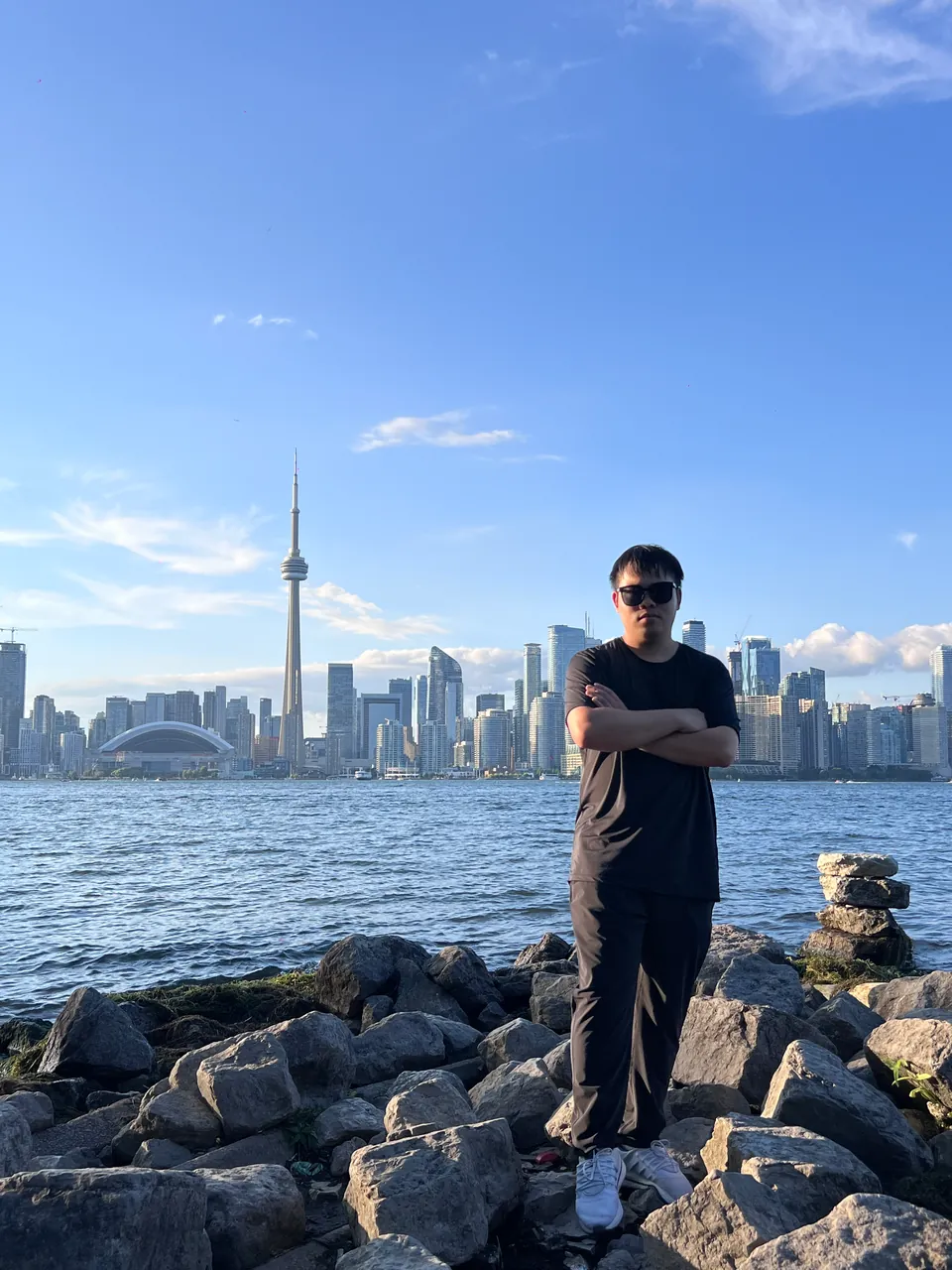 Jinhao on lakeshore rocks with the Toronto skyline and the CN Tower across the water