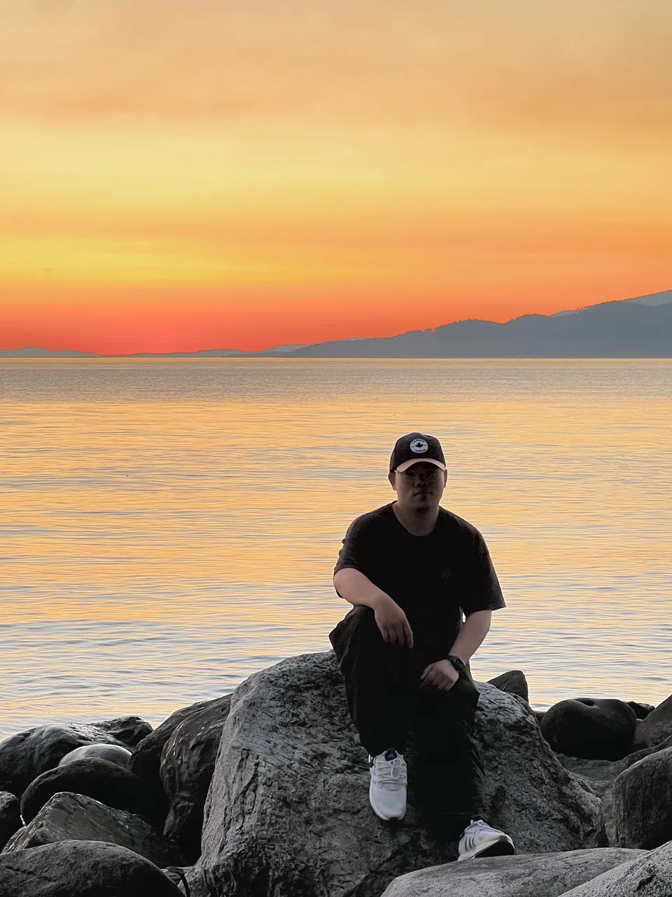 Jinhao sitting on beach rocks under an orange sunset sky