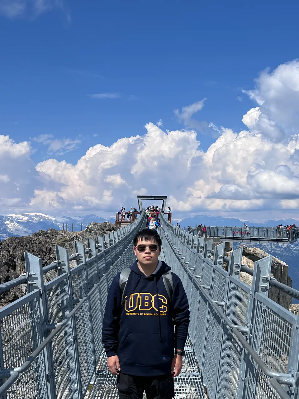 Jinhao on a metal suspension bridge at a mountain top under big white clouds